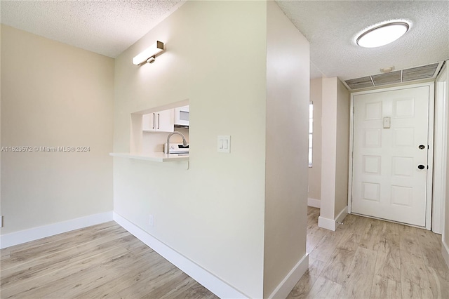 hallway with sink, a textured ceiling, and light hardwood / wood-style floors