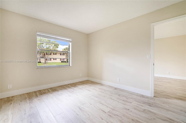 empty room with a textured ceiling and light hardwood / wood-style floors