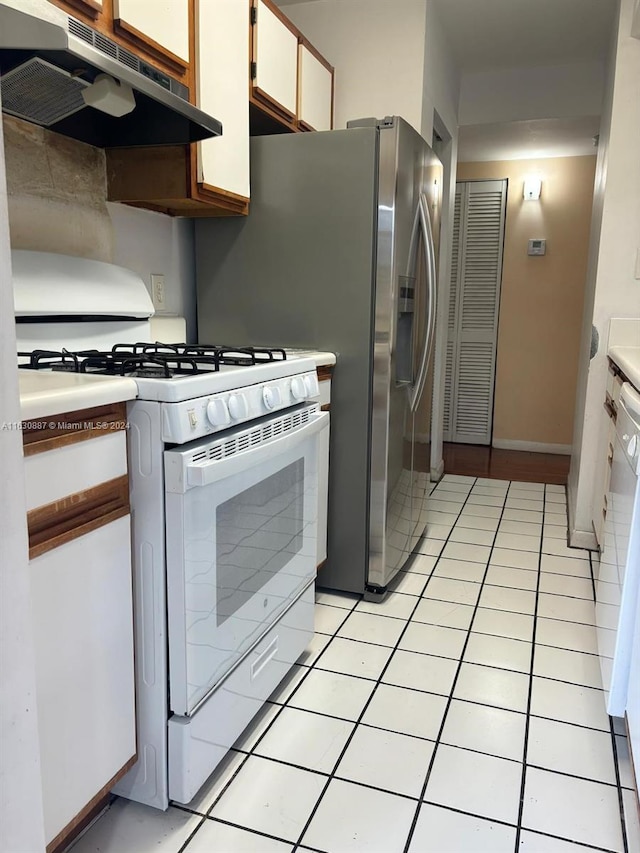 kitchen with light tile patterned flooring, white gas range oven, and white cabinets