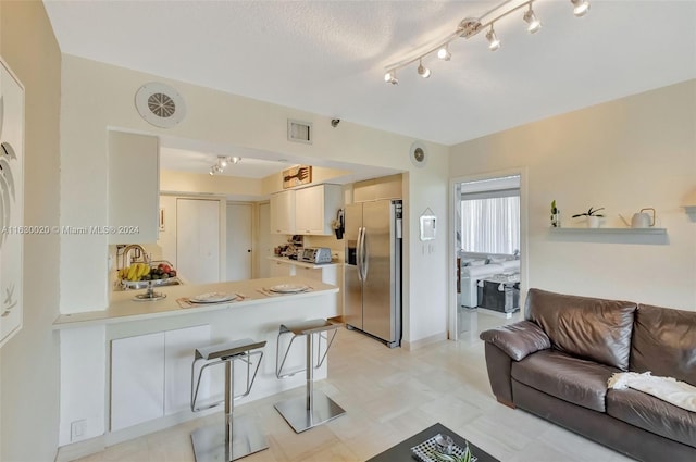 kitchen featuring stainless steel fridge with ice dispenser, kitchen peninsula, a kitchen breakfast bar, light tile patterned floors, and track lighting