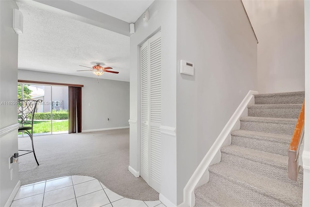 staircase featuring light carpet, a textured ceiling, and ceiling fan