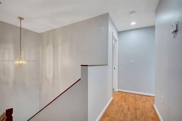 hall featuring a chandelier, light wood-type flooring, and a textured ceiling