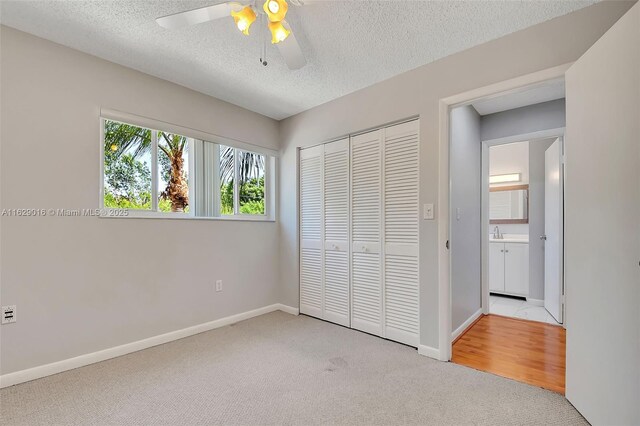 unfurnished bedroom featuring light carpet, a textured ceiling, a closet, and ceiling fan