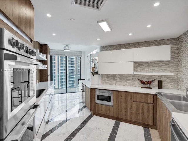 kitchen with appliances with stainless steel finishes, tasteful backsplash, white cabinets, sink, and light tile patterned floors