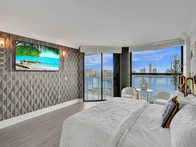 bedroom with hardwood / wood-style floors, access to exterior, a water view, expansive windows, and crown molding