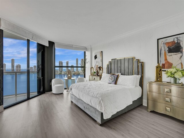 bedroom featuring access to exterior, a water view, expansive windows, and wood-type flooring