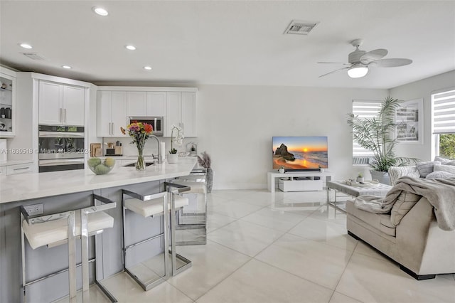 kitchen featuring double oven, a breakfast bar area, white cabinets, and ceiling fan