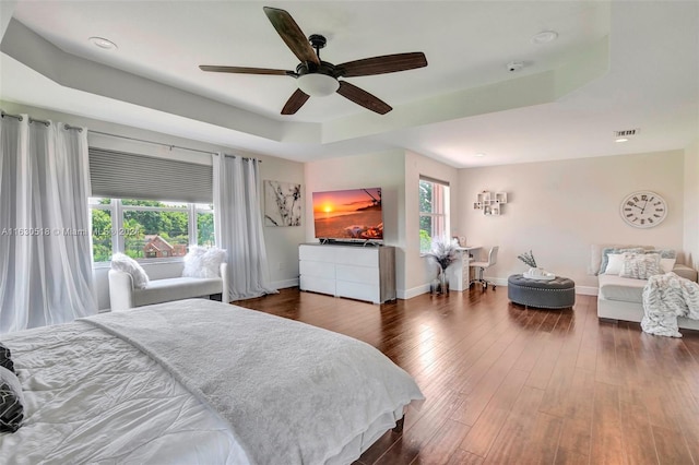 bedroom featuring a raised ceiling, ceiling fan, dark hardwood / wood-style floors, and multiple windows