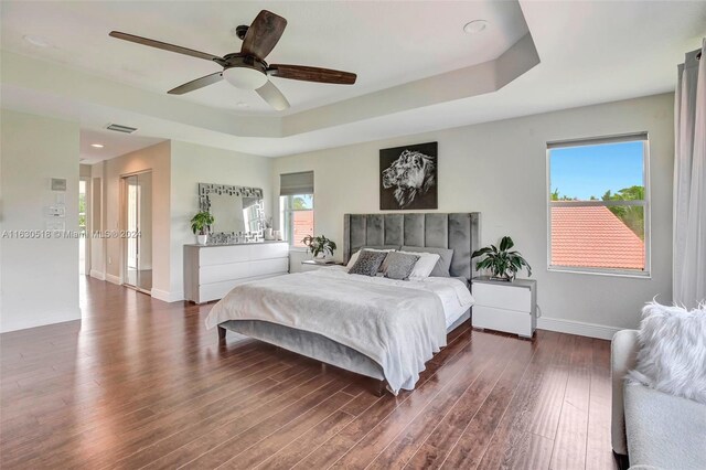 bedroom featuring dark wood-type flooring, a tray ceiling, a closet, and ceiling fan