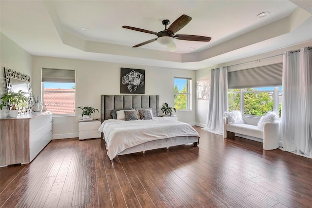 bedroom with ceiling fan, dark hardwood / wood-style flooring, and a tray ceiling