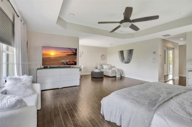 bedroom with ceiling fan, a tray ceiling, and dark hardwood / wood-style flooring