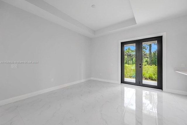 spare room featuring marble finish floor, baseboards, a raised ceiling, and french doors