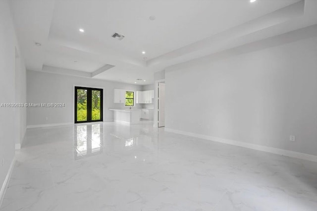 unfurnished living room featuring a tray ceiling, french doors, and baseboards