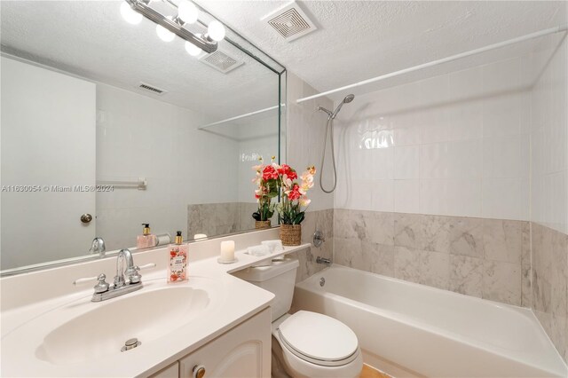 full bathroom featuring toilet, tiled shower / bath combo, vanity, and a textured ceiling