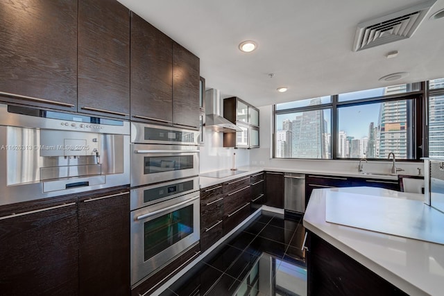 kitchen featuring wall chimney range hood, sink, dark brown cabinetry, black electric stovetop, and dark tile patterned flooring