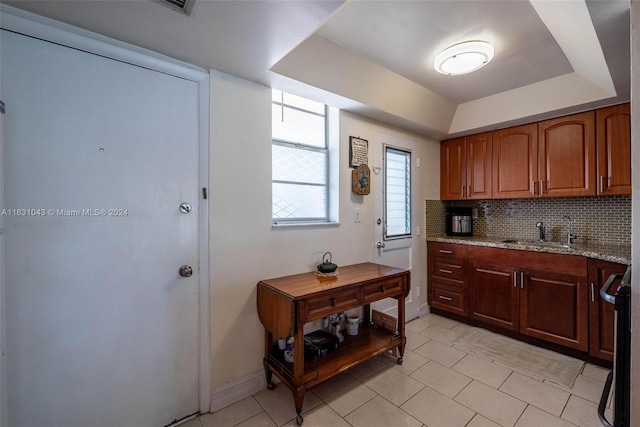 kitchen with light tile patterned flooring, tasteful backsplash, a tray ceiling, sink, and light stone counters