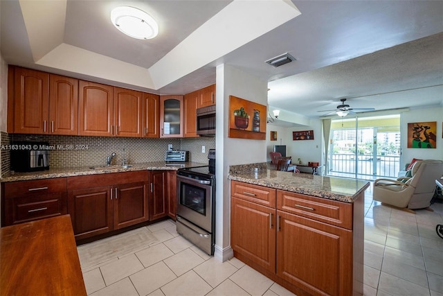 kitchen with light stone counters, ceiling fan, stainless steel appliances, a raised ceiling, and sink