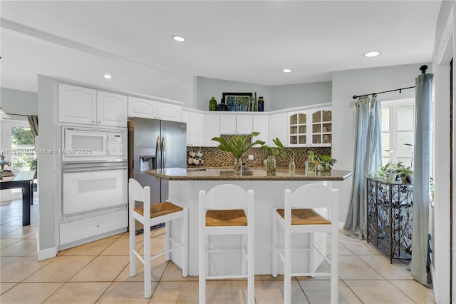 kitchen with a breakfast bar, tasteful backsplash, white cabinetry, white appliances, and glass insert cabinets