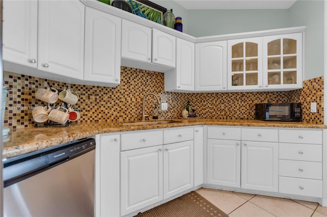 kitchen featuring glass insert cabinets, dishwasher, light tile patterned floors, decorative backsplash, and a sink