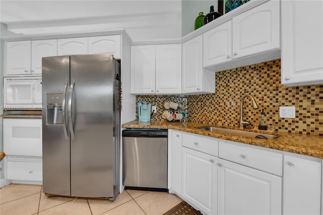 kitchen with light tile patterned flooring, white cabinets, stone countertops, stainless steel appliances, and a sink