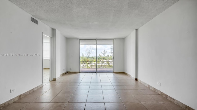 spare room featuring light tile patterned flooring, a wall of windows, and a textured ceiling