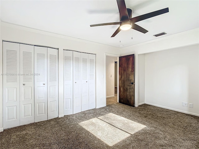 unfurnished bedroom featuring carpet floors, multiple closets, crown molding, and ceiling fan