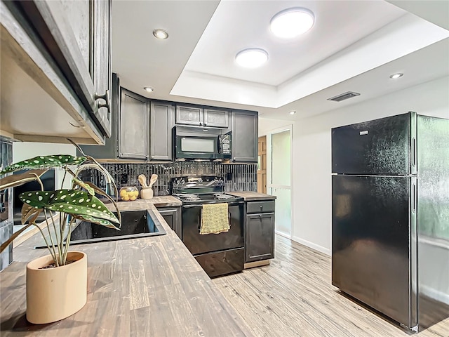 kitchen with black appliances, tasteful backsplash, a raised ceiling, light hardwood / wood-style flooring, and gray cabinetry