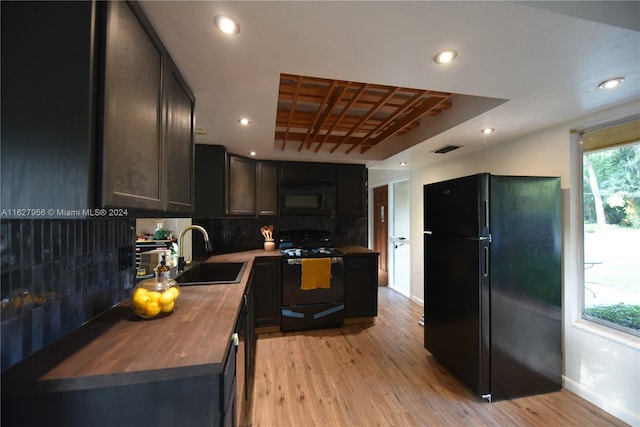 kitchen with black appliances, wooden counters, sink, light hardwood / wood-style flooring, and backsplash