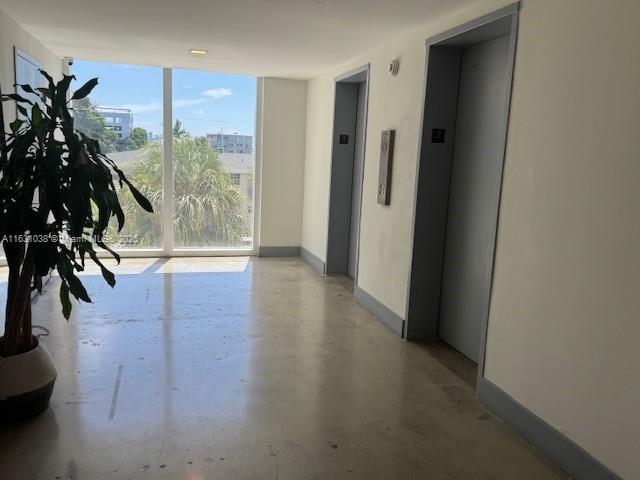 interior space with a wall of windows, elevator, finished concrete flooring, and baseboards