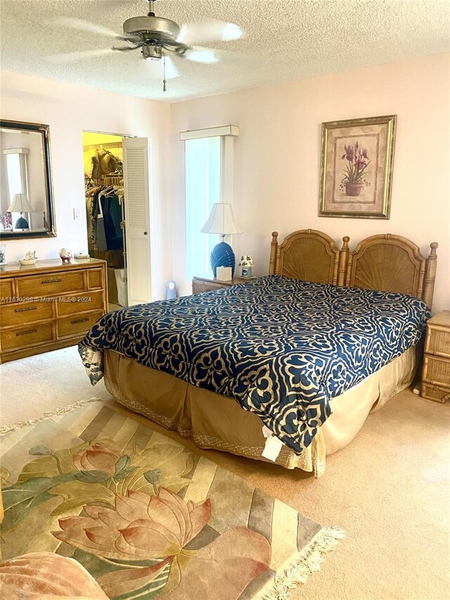 carpeted bedroom with a closet, a textured ceiling, a spacious closet, and a ceiling fan