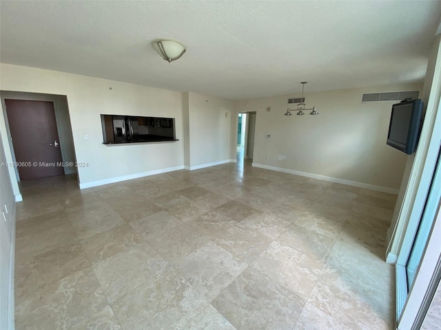 unfurnished living room with light tile patterned flooring, a textured ceiling, and a notable chandelier