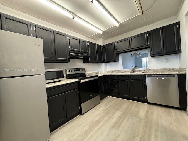 kitchen with light wood-type flooring, light stone countertops, stainless steel appliances, and sink