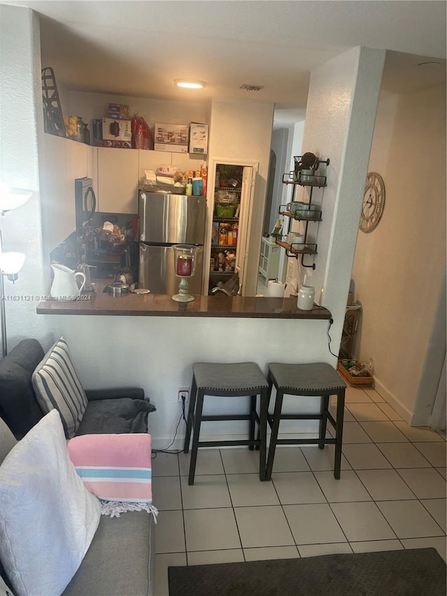 kitchen featuring kitchen peninsula, stainless steel refrigerator, light tile patterned floors, a kitchen breakfast bar, and white cabinetry