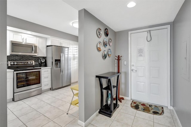 kitchen featuring decorative backsplash, white cabinetry, stainless steel appliances, and light tile patterned floors