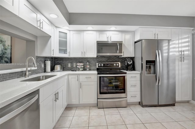 kitchen featuring decorative backsplash, stainless steel appliances, sink, light tile patterned floors, and white cabinets