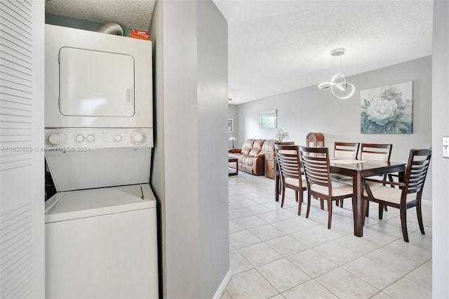 clothes washing area featuring stacked washer / drying machine, a notable chandelier, a textured ceiling, and light tile patterned floors