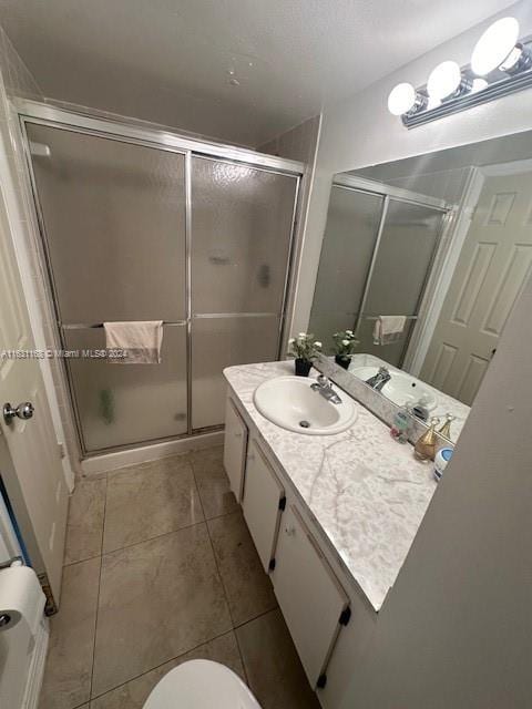 bathroom featuring a shower with door, toilet, vanity, and tile patterned floors