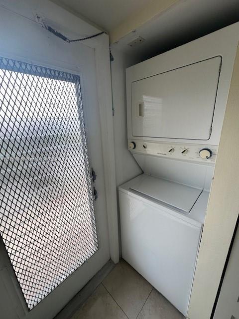 laundry area with stacked washing maching and dryer and light tile patterned floors