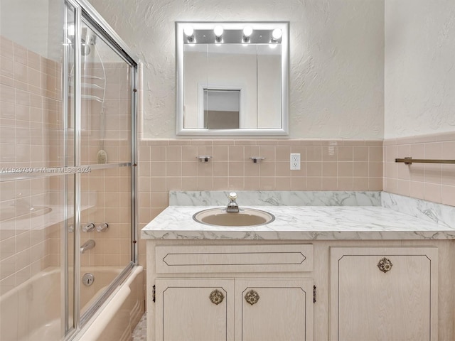 bathroom with vanity, enclosed tub / shower combo, and tile walls