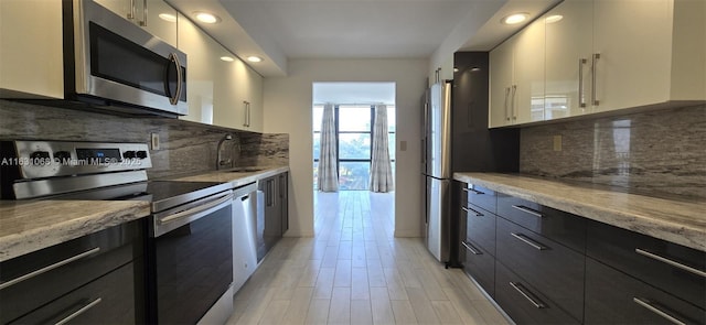 kitchen featuring sink, light stone counters, light hardwood / wood-style flooring, appliances with stainless steel finishes, and backsplash