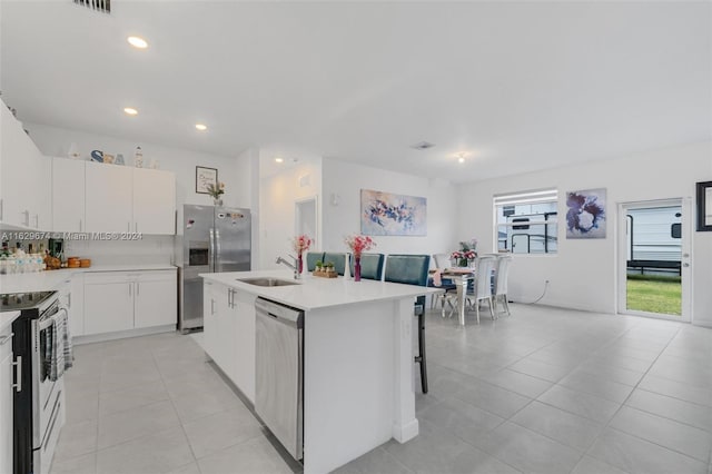 kitchen featuring white cabinets, stainless steel appliances, sink, light tile patterned floors, and an island with sink