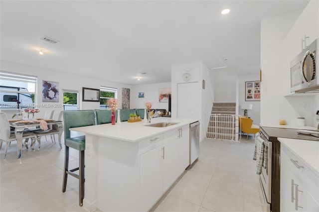 kitchen with white cabinets, an island with sink, sink, appliances with stainless steel finishes, and light tile patterned floors