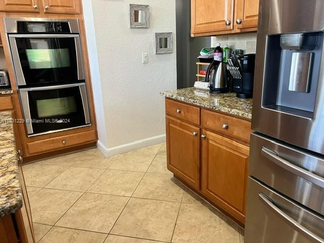 kitchen with light stone counters, light tile patterned floors, tasteful backsplash, and appliances with stainless steel finishes