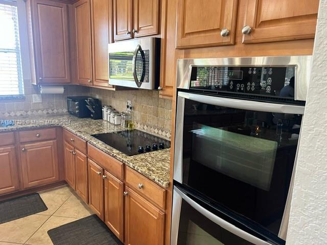 kitchen featuring light stone countertops, backsplash, light tile patterned flooring, and appliances with stainless steel finishes