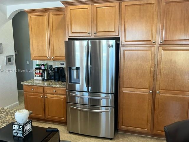 kitchen featuring stainless steel refrigerator with ice dispenser, light tile patterned floors, tasteful backsplash, and stone counters