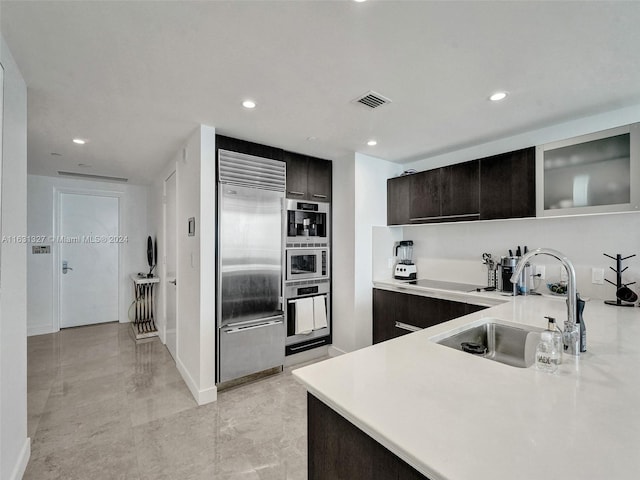 kitchen with dark brown cabinetry, built in appliances, sink, and light tile patterned floors