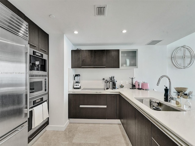 kitchen featuring light tile patterned floors, dark brown cabinetry, sink, and built in appliances