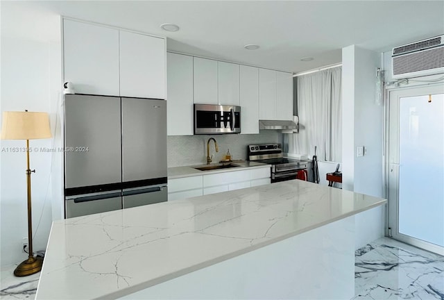 kitchen with wall chimney range hood, white cabinets, stainless steel appliances, light stone countertops, and sink