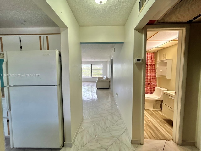 hall with a textured ceiling and light hardwood / wood-style flooring