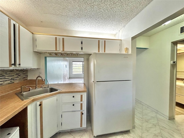 kitchen with white fridge, white cabinetry, and sink